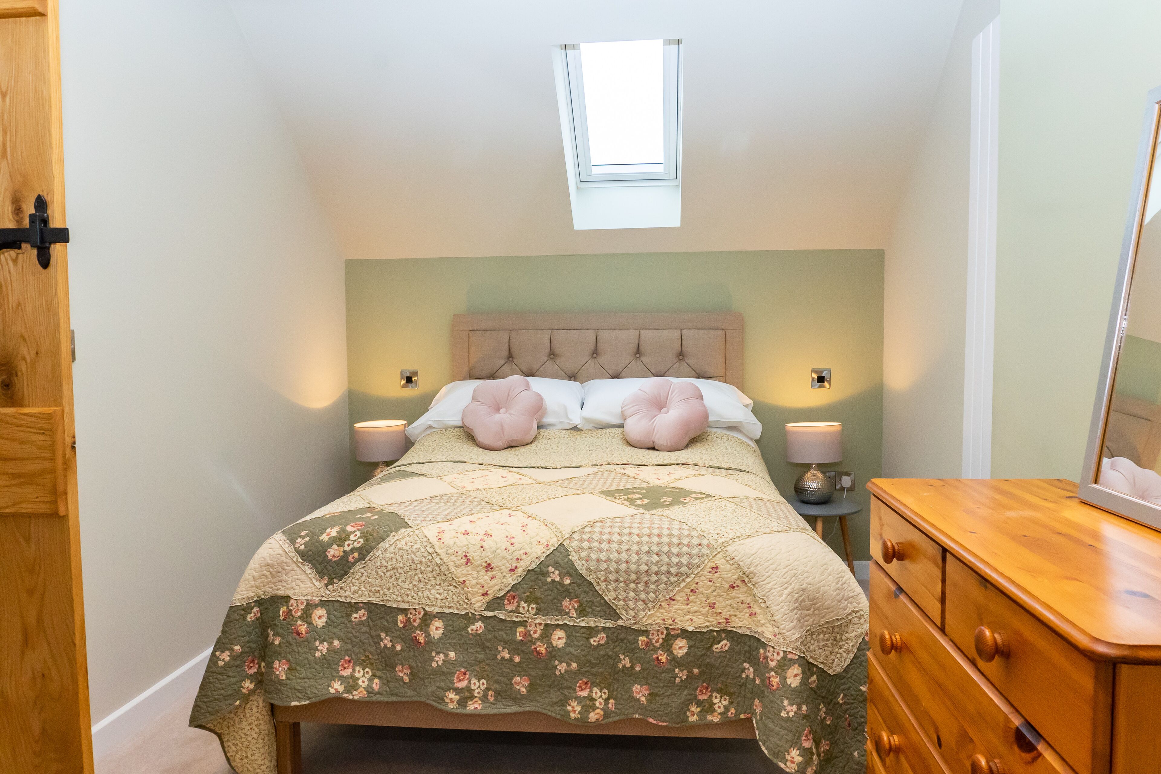 Um quarto com cama, penteadeira, mesa de cabeceira, janela e porta.