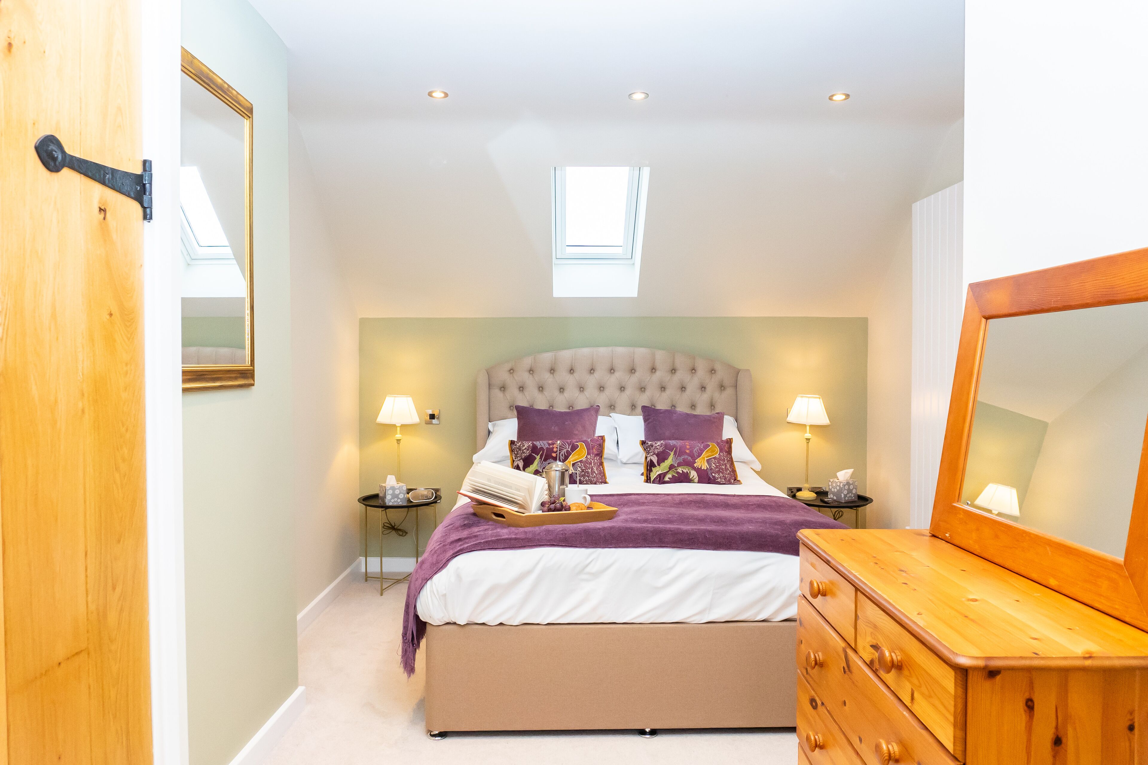 Une chambre à coucher comprenant un lit, des tables de chevet, une commode, un miroir et une fenêtre de toit.