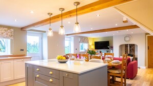 A spacious kitchen with a central island, wooden beams, pendant lighting, and a dining area with a red sofa and wooden chairs. - The Patches (Shrewsbury)
