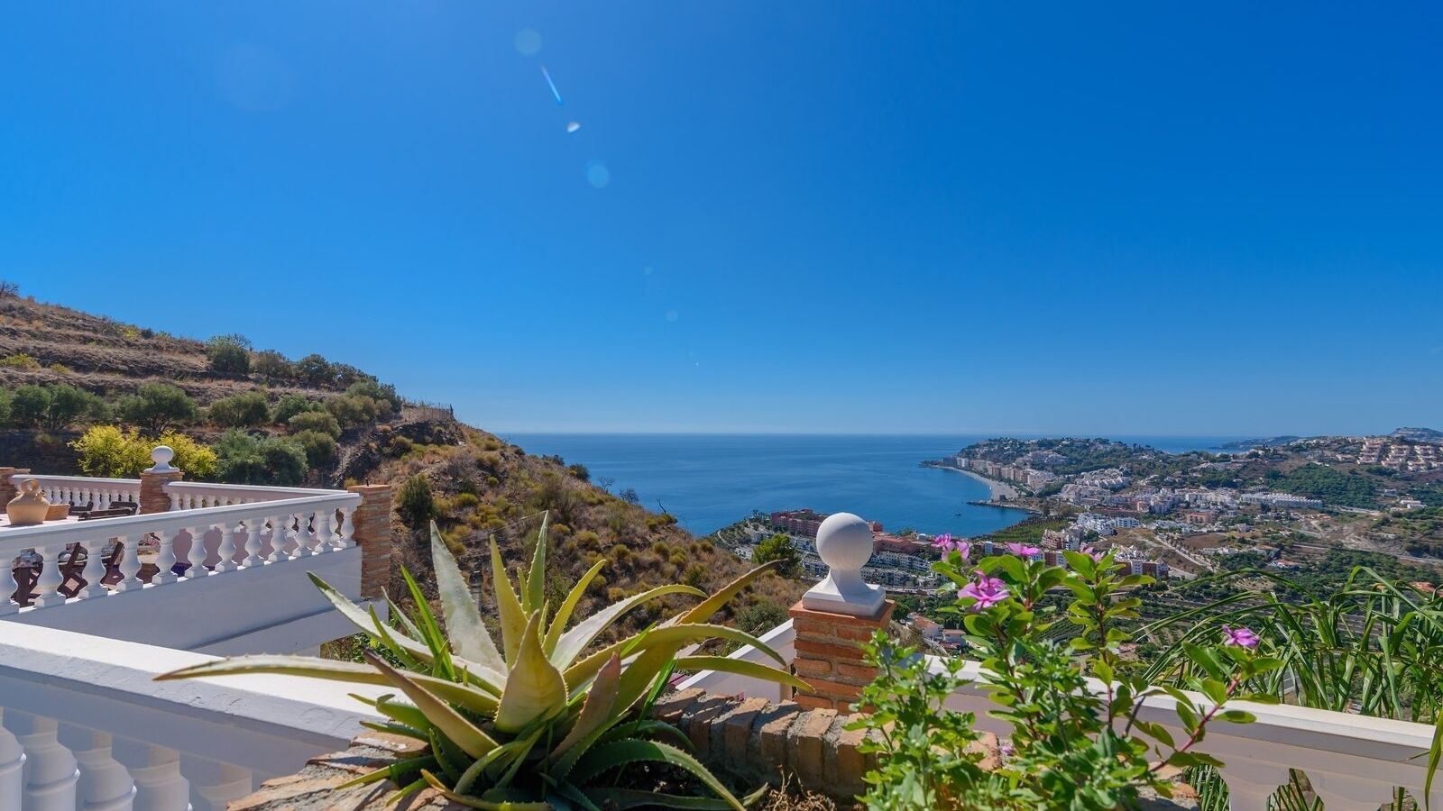 A coastal view with a white balustrade, a white spherical object, and green foliage.