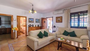A living room with two sofas, a coffee table, a chandelier, and a dining area with a chair and table. - Villa Turistica Almuñécar by Ruralidays (Granada)