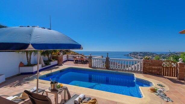A swimming pool with a view of the sea, a patio with a table and chairs, and a covered area with an umbrella. - Villa Turistica Almuñécar by Ruralidays (Granada)