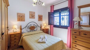 A bedroom with a bed, bedside tables, a dresser, a window with curtains, and wall art. - Villa Turistica Almuñécar by Ruralidays (Granada)