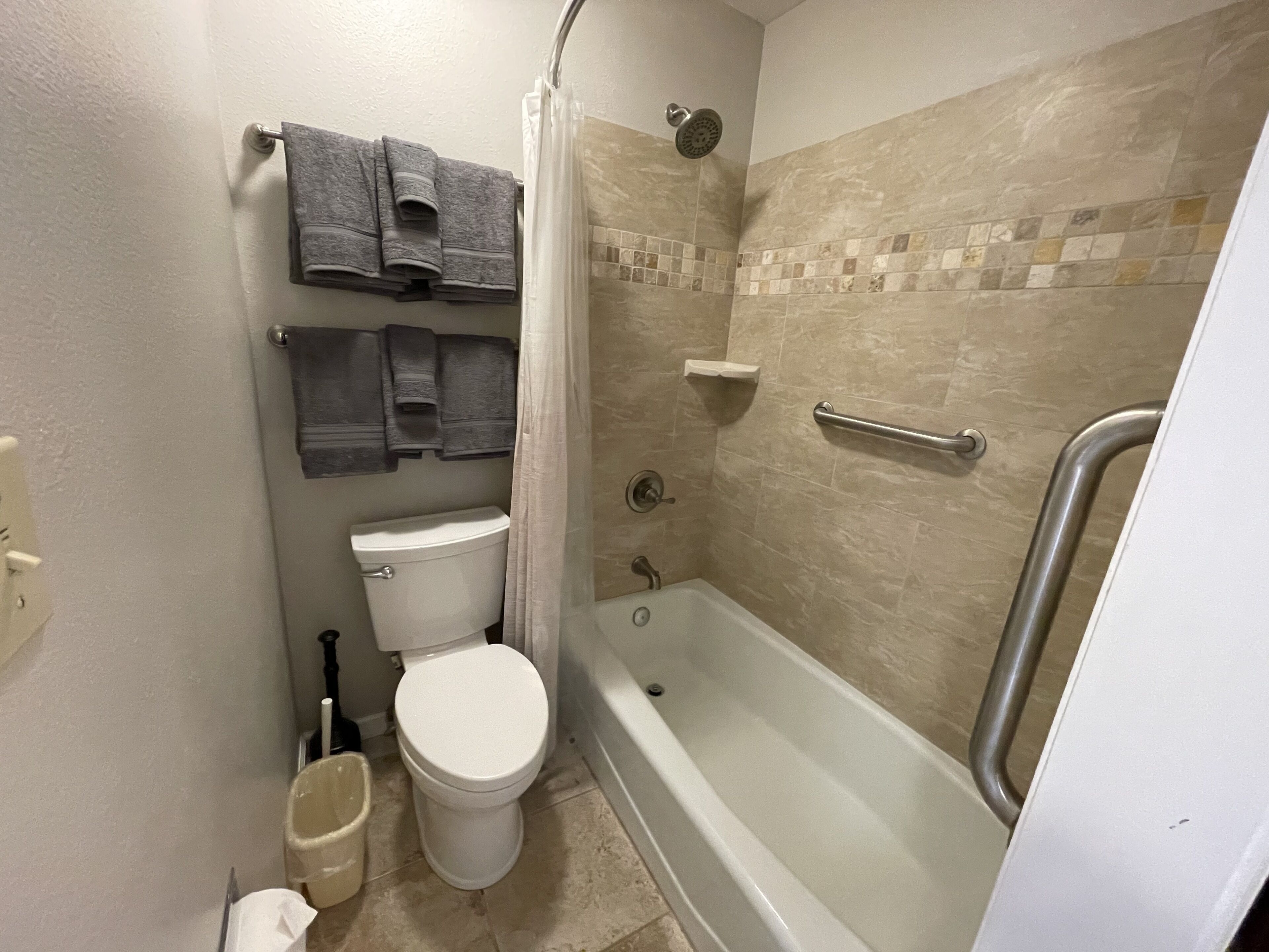 A bathroom with a toilet, bathtub, shower, and a towel rack.