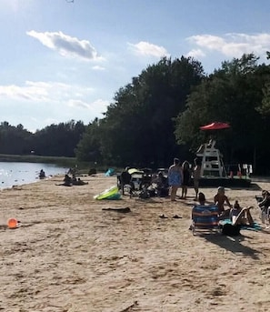 Une plage avec des gens, une tour de surveillance pour les sauveteurs et un lac en arrière-plan.