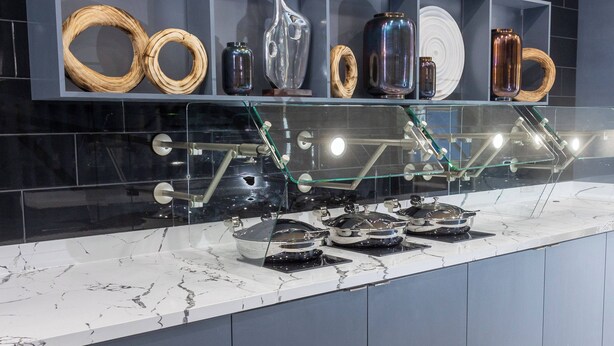 A kitchen with marble countertops, a glass display case with various kitchenware, and a modern backsplash. - SpringHill Suites by Marriott Slidell (Slidell)