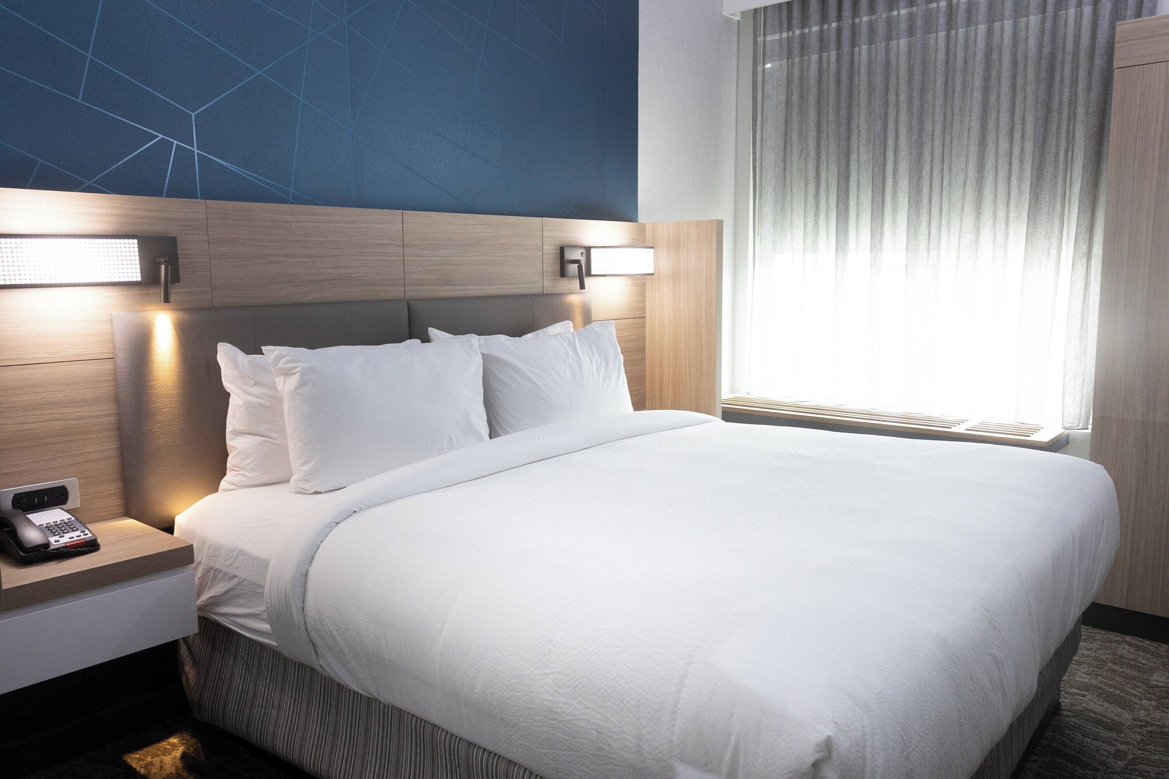 A hotel room with a large bed, a bedside table with a phone, and a wall-mounted light fixture.