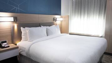 A hotel room with a large bed, a bedside table with a phone, and a wall-mounted light fixture.