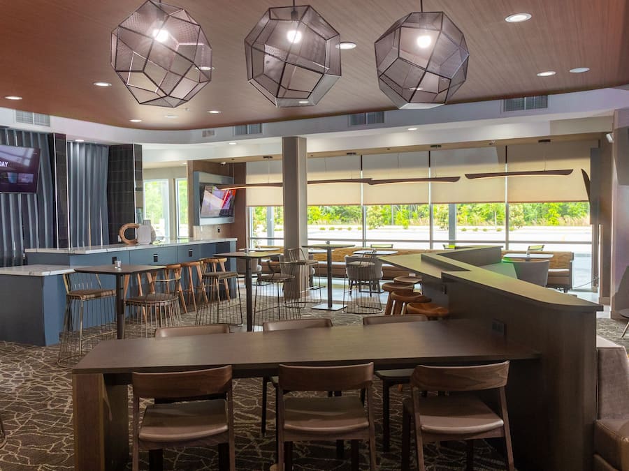 A modern restaurant with a central bar, multiple seating areas, and large windows offering a view of the outdoors.