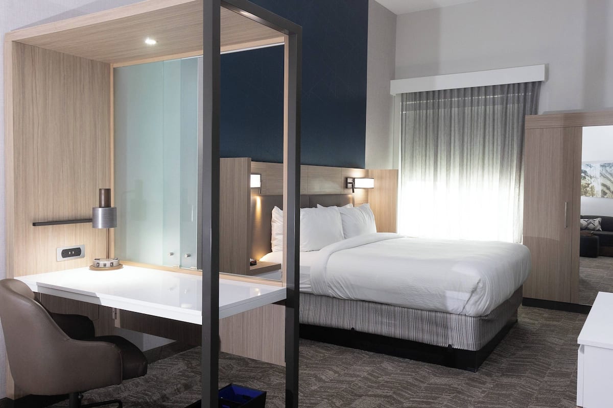 A hotel room with a bed, a desk, a chair, a lamp, and a window with curtains.