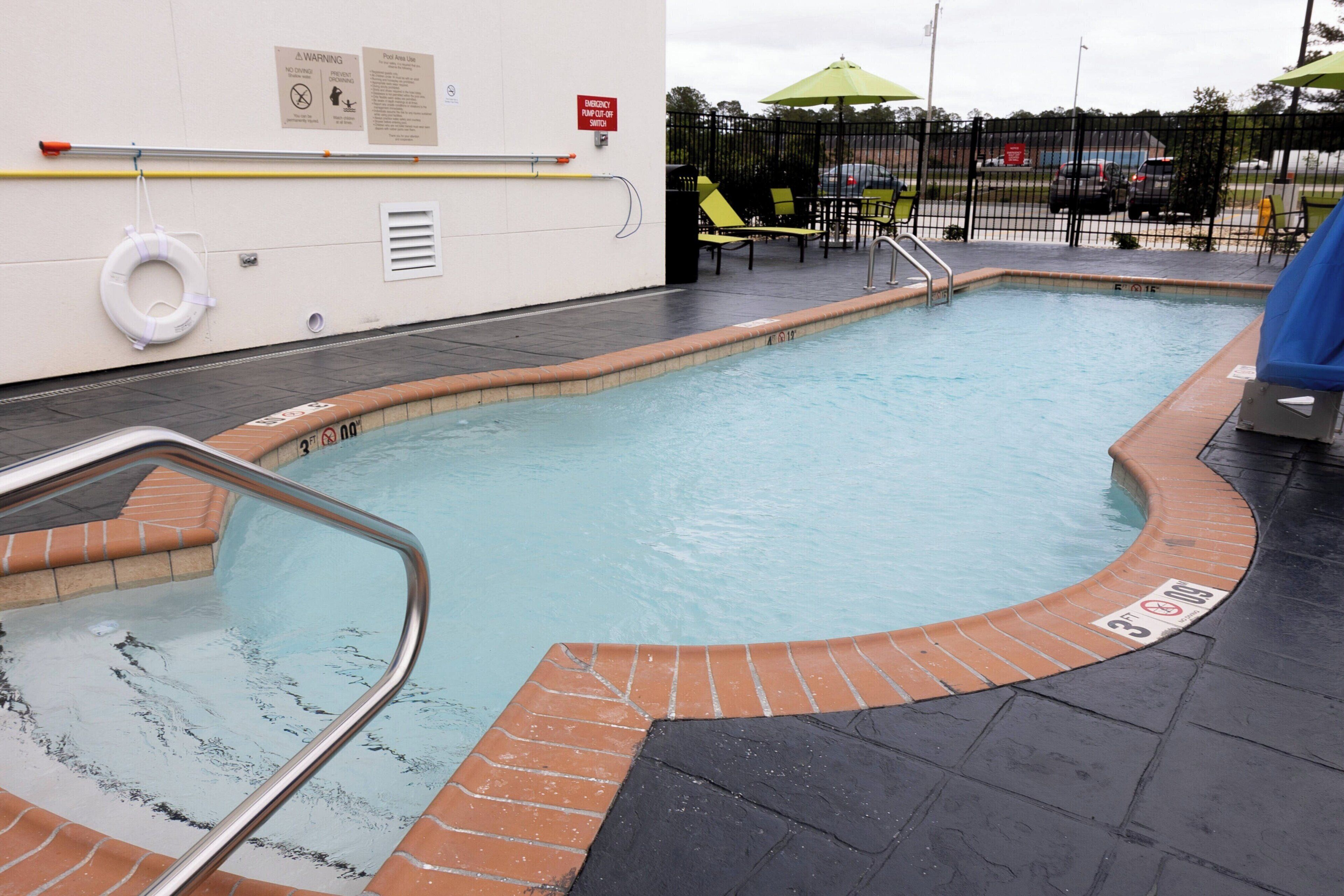 Una piscina con borde de ladrillo, un flotador salvavidas y un letrero de advertencia en la pared.