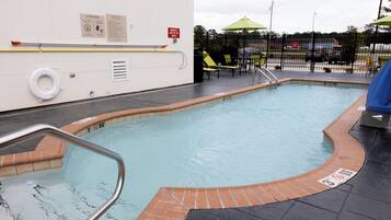 Una piscina con borde de ladrillo, un flotador salvavidas y un letrero de advertencia en la pared.