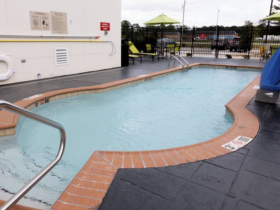 Una piscina con borde de ladrillo, un flotador salvavidas y un letrero de advertencia en la pared.