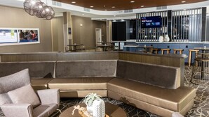 A modern hotel lobby with a curved seating area, a bar with stools, and a digital screen displaying a message. - SpringHill Suites by Marriott Slidell (Slidell)