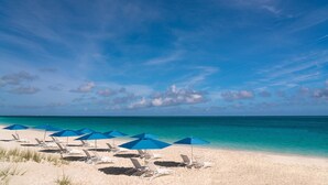 A beach with white lounge chairs and blue umbrellas, a clear sky, and turquoise water. - The Ritz-Carlton, Turks & Caicos (Providenciales)