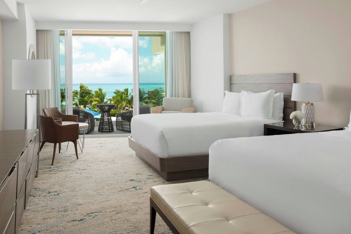 A hotel room with two beds, a desk, a chair, and a view of the ocean.