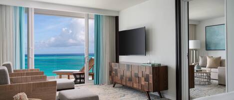 Hotelkamer met groot raam met uitzicht op de oceaan, een flatscreen televisie aan de wand, een houten console tafel, een bank en een bed.
