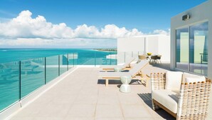 A balcony with a clear view of the ocean, lounge chairs, and a dining area.
