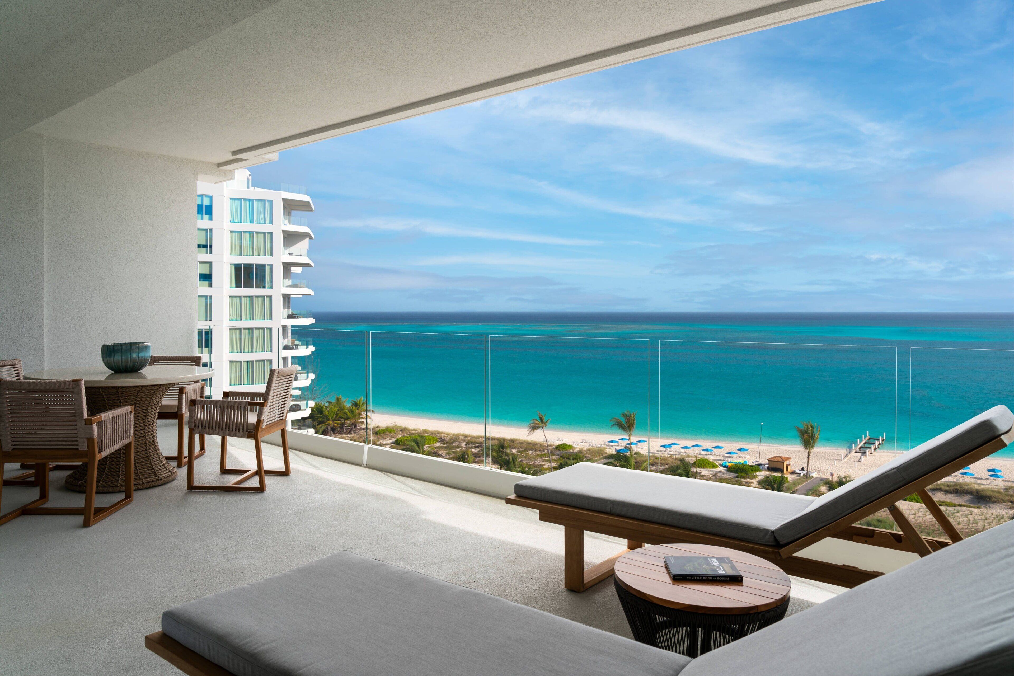 A balcony with a view of the ocean, a dining area with wicker furniture, and a lounge area with a cushioned bench and a small table.
