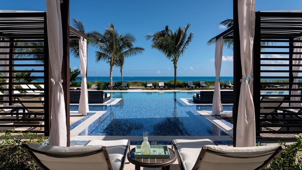 A poolside area with lounge chairs, a table with a drink, and a view of the ocean. - The Ritz-Carlton, Turks & Caicos (Providenciales)