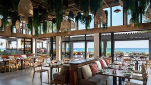 A restaurant with a view of the ocean, featuring hanging wicker chandeliers, wooden furniture, and a bar area. - The Ritz-Carlton, Turks & Caicos (Providenciales)