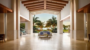 A spacious lobby with a central seating area, large pillars, and a view of palm trees and a beach. - The Ritz-Carlton, Turks & Caicos (Providenciales)