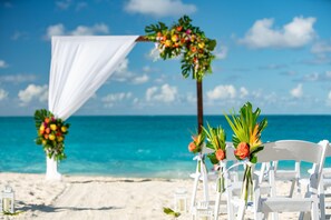 A beach wedding setup with white chairs and floral decorations.