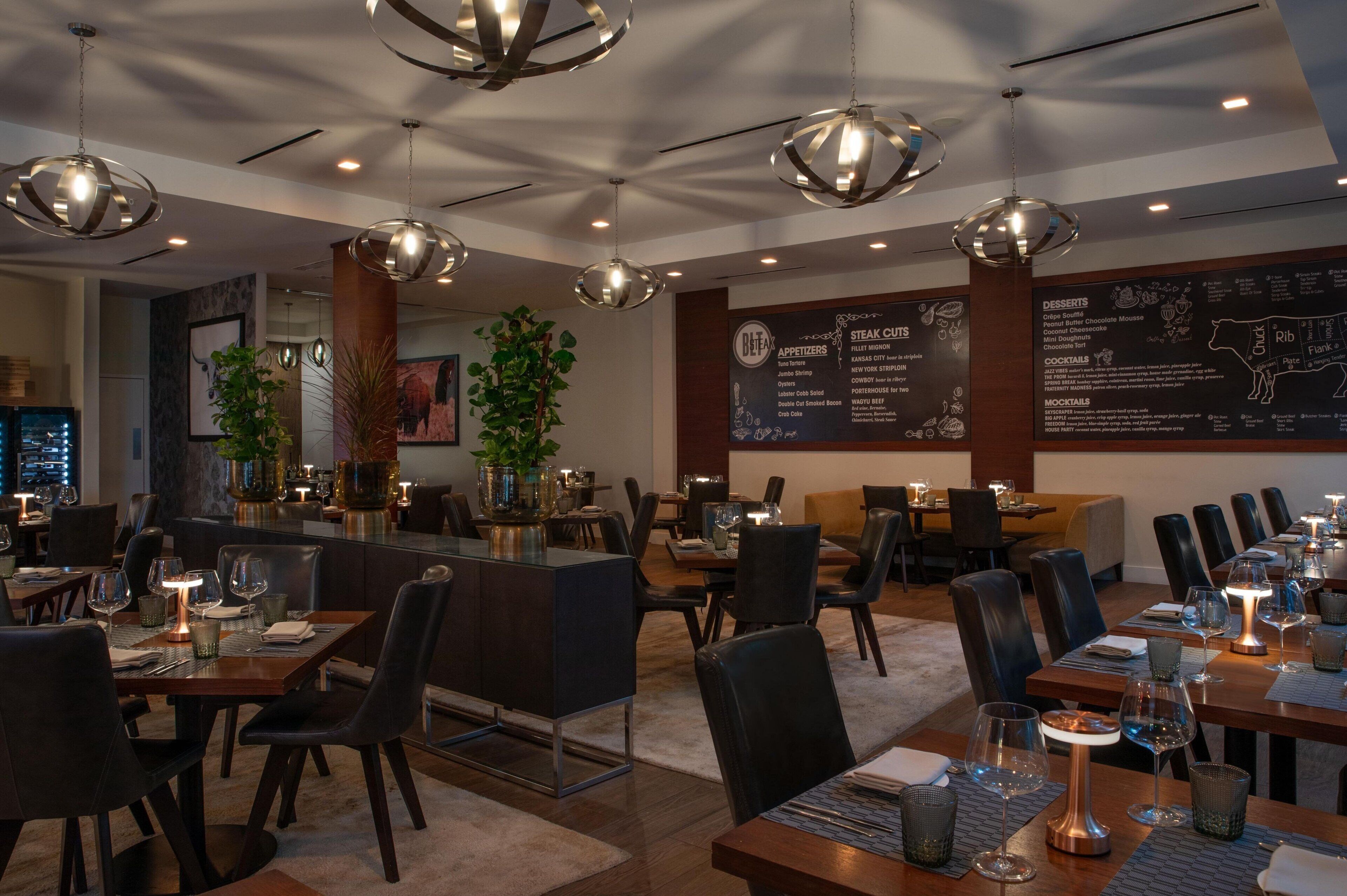 A restaurant with multiple dining tables, black chairs, and hanging spherical light fixtures.
