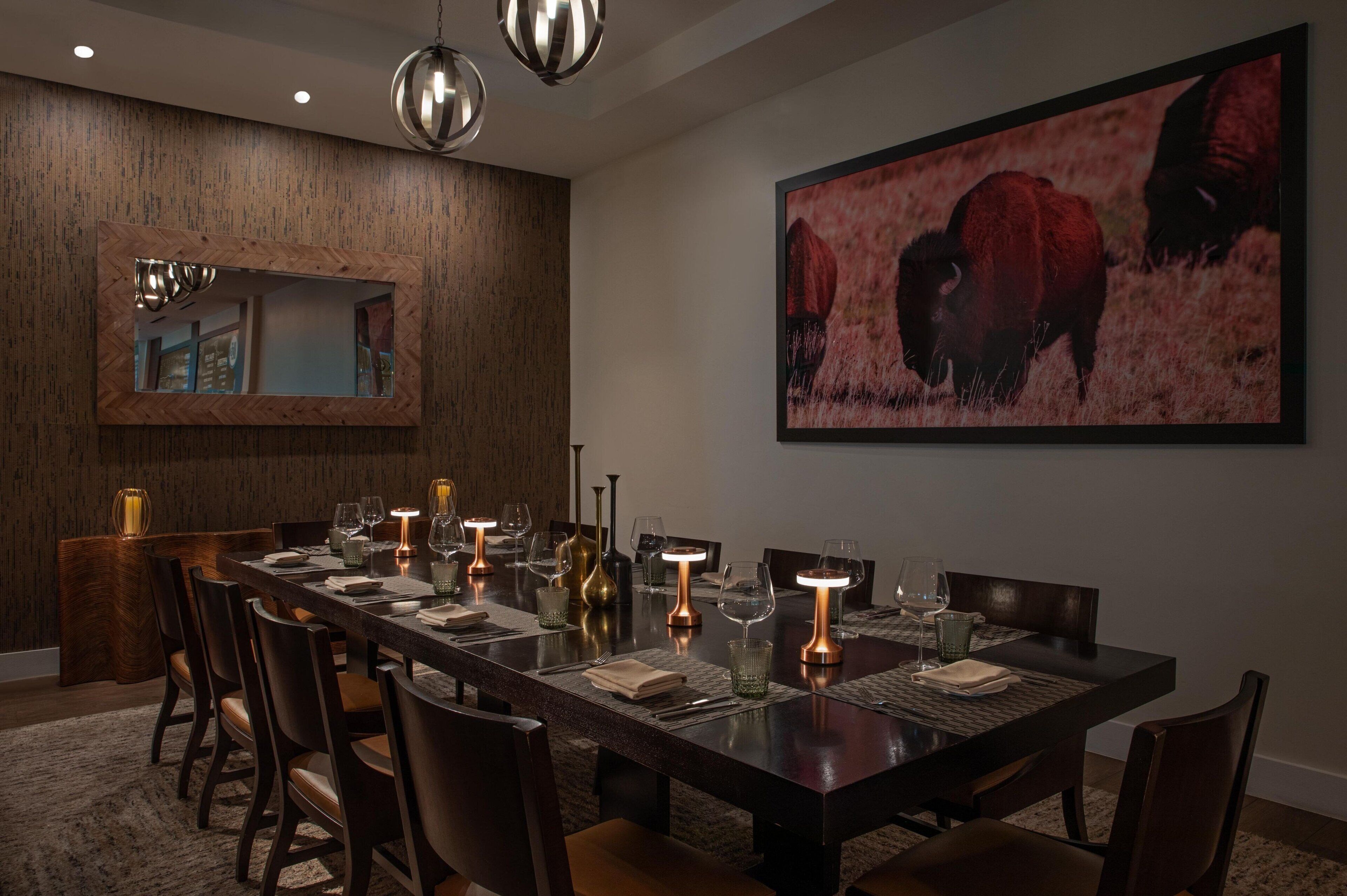 Un comedor con una mesa larga dispuesta para seis personas, rodeada de sillas, con un cuadro grande enmarcado de bisontes en la pared.
