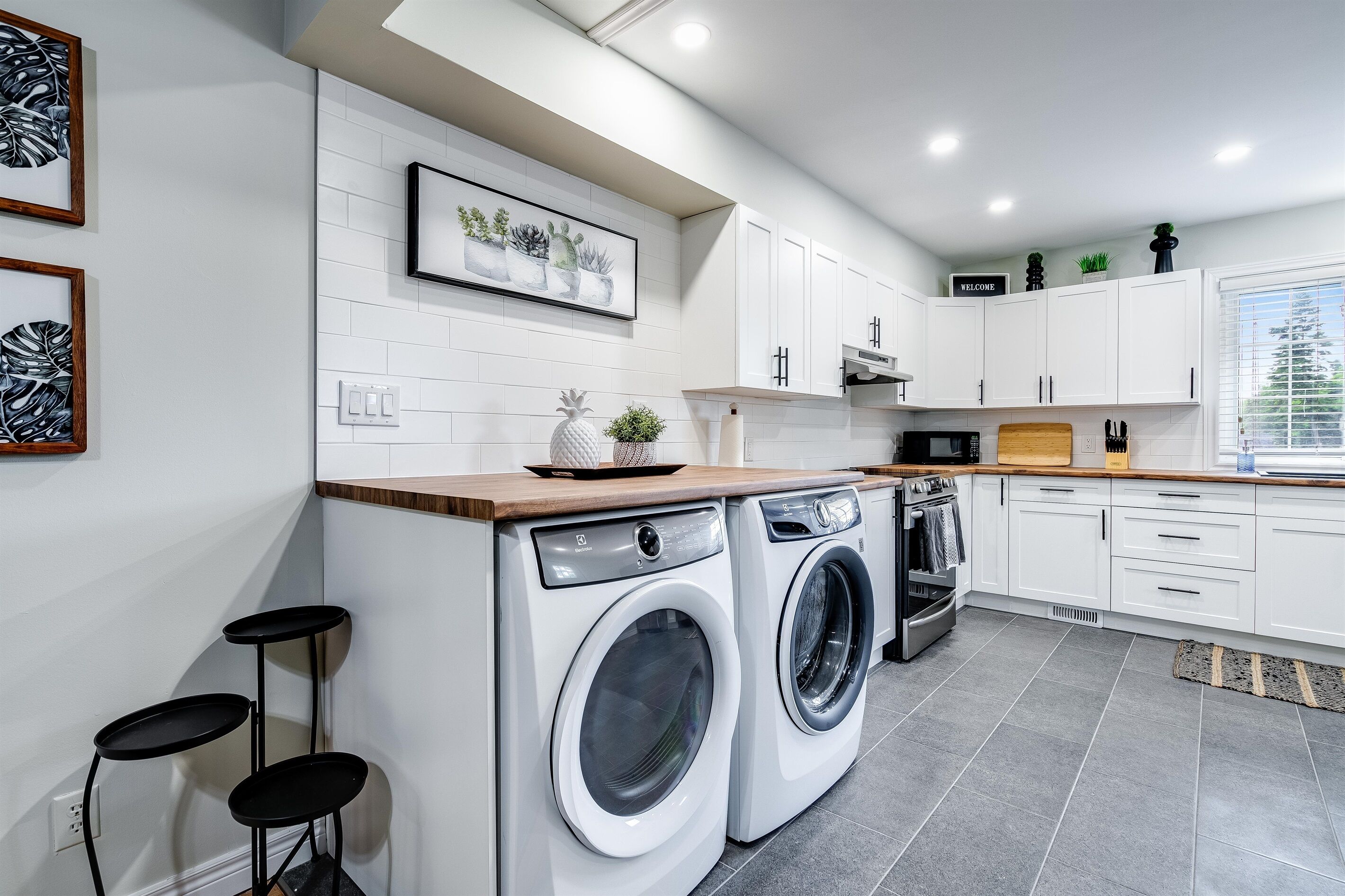 Une cuisine moderne avec des armoires blanches, un lave-linge encastré, un four à micro-ondes et un plan de travail en bois.