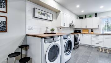 Une cuisine moderne avec des armoires blanches, un lave-linge encastré, un four à micro-ondes et un plan de travail en bois.