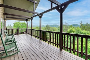 Una terraza de madera con barandilla, un espacio cubierto y vistas a un paisaje boscoso.