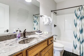 Ein Badezimmer mit Marmorwaschbecken, Holzschränken, einer weißen Toilette und einer Dusche mit gemusterten Vorhängen.