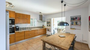 Une cuisine avec des meubles de rangement en bois, une table à manger et un luminaire suspendu noir.
