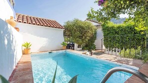 Une piscine rectangulaire dont le bord est recouvert de carreaux, entourée d’une terrasse en bois et agrémentée de plantes en pot.