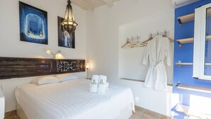 Une chambre d’hôtel comprenant un lit, une tête de lit, une lampe fixée au mur, un tableau, un porte-peignoir et une fenêtre.