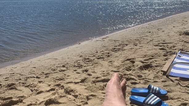 Una playa con huellas en la arena, un par de chanclas azules y una silla de playa.