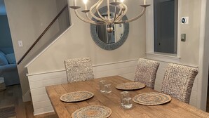 Un comedor con mesa de madera, sillas tejidas, una araña y un espejo en la pared.