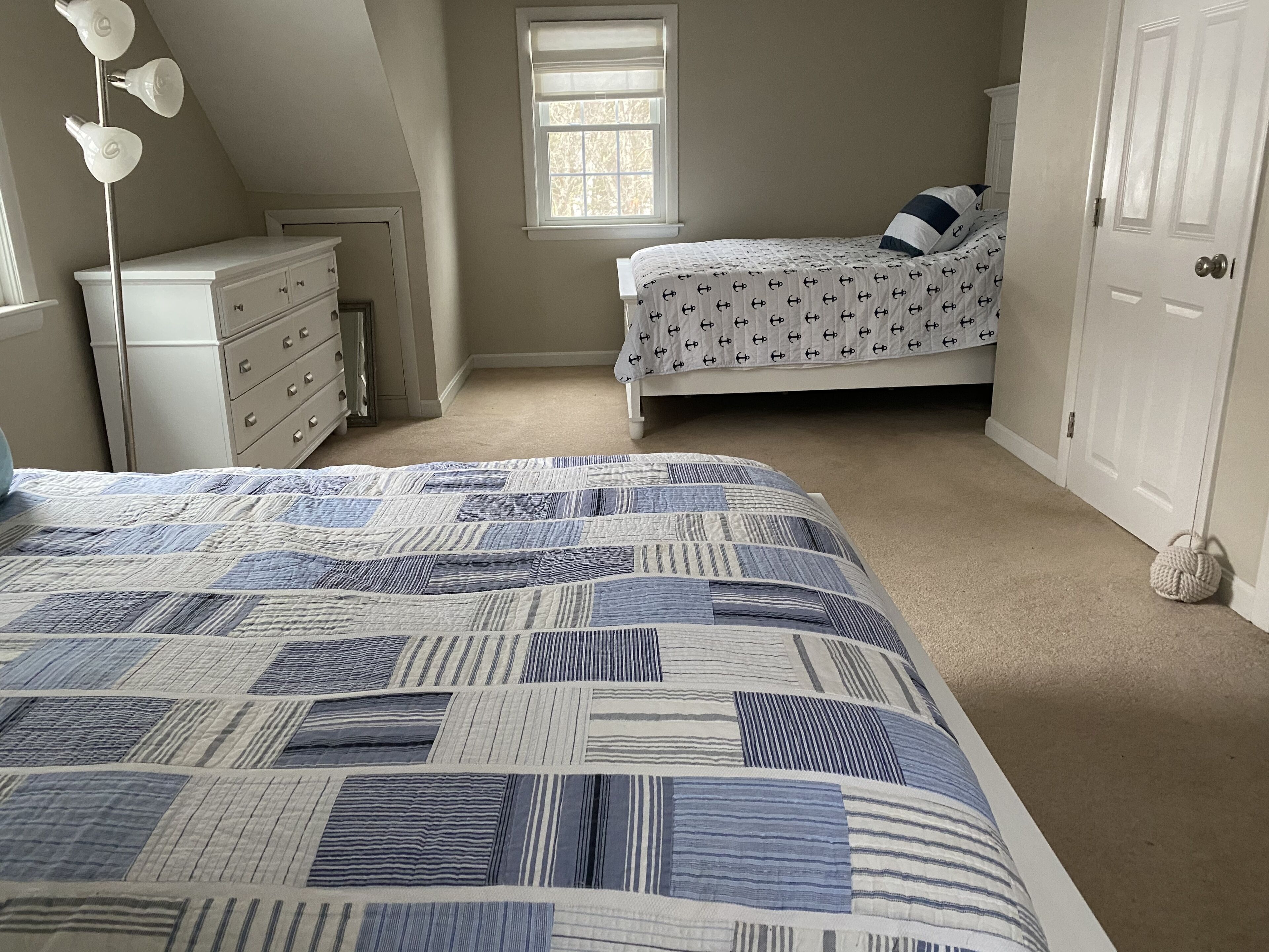 A bedroom with a large bed, a dresser, a window, and a door.