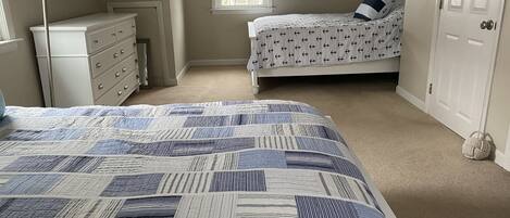 A bedroom with a large bed, a dresser, a window, and a door.