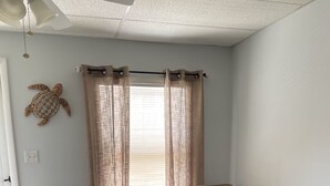 A living room with a beige sofa, two patterned pillows, a small wooden side table, and a decorative turtle wall art piece. - Bradley Beach Quaint Getaway (Bradley Beach)