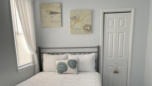 A bedroom with a large bed, a window with curtains, a door, and two wall art pieces. - Bradley Beach Quaint Getaway (Bradley Beach)