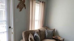 A beige sofa with patterned cushions, a small wooden side table, a remote control, and a decorative turtle on the wall. - Bradley Beach Quaint Getaway (Bradley Beach)