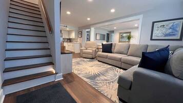 Un salon moderne avec un escalier, un canapé, une table basse et un coin cuisine à l’arrière-plan.