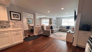 A modern kitchen with white cabinets, a dining area with a table and chairs, a living room with a sofa and a coffee table, and a large window providing natural light. - Oatland Island Family Cottage 10 minutes from Tybee Island and Historic Savannah (Savannah)