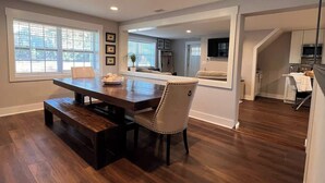 A spacious living area with a wooden dining table, a bench, and a chair. There is a kitchen in the background with modern appliances. - Oatland Island Family Cottage 10 minutes from Tybee Island and Historic Savannah (Savannah)