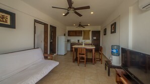 Uma sala de estar com sofá, mesa de jantar com cadeiras, ventilador de teto e televisão.