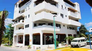 Um hotel de vários andares com fachada branca, varandas e telhado de palha.