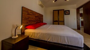 Quarto com cama, mesa de cabeceira, ventilador de teto e ar condicionado fixado na parede.