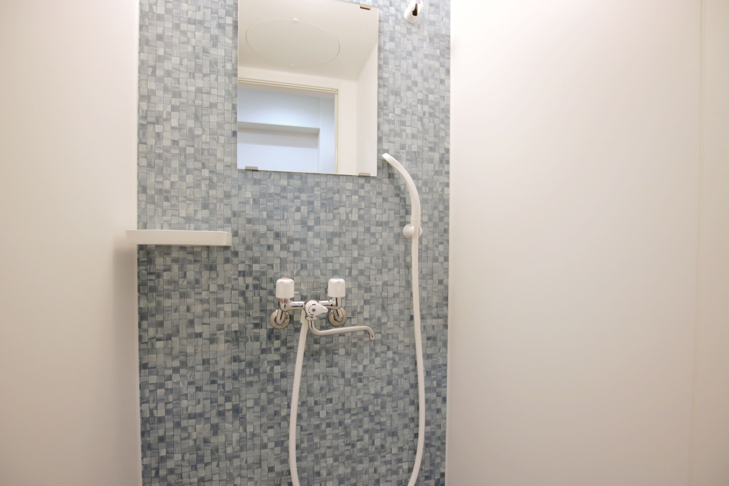 Casa de banho com chuveiro, espelho e parede revestida a azulejos.